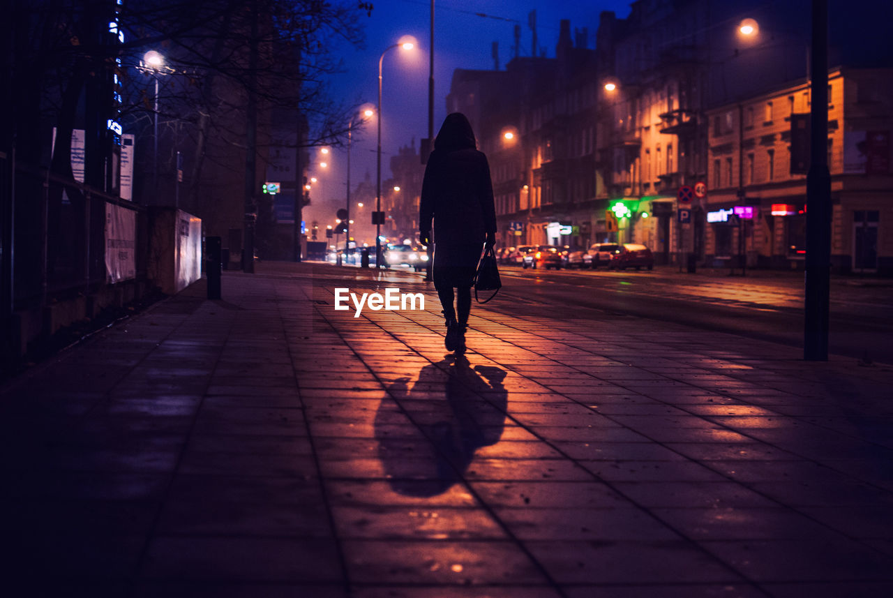 Rear view of silhouette woman walking on footpath in city at night