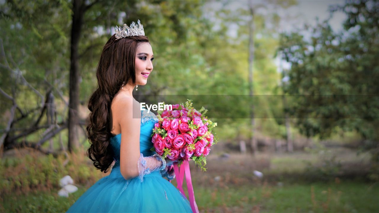 Side view of bride holding bouquet while standing at park