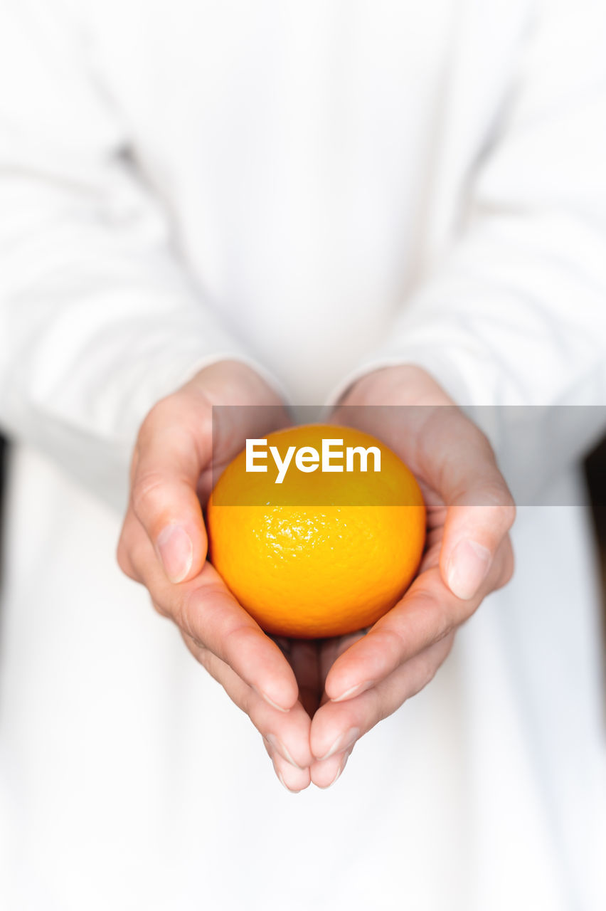 Girl in a white sweater holds a fresh sweet tangerine against the background of herself in defocus