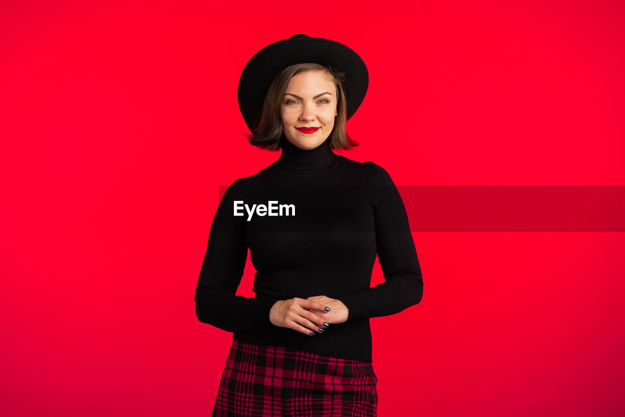 Portrait of smiling young woman standing against red background