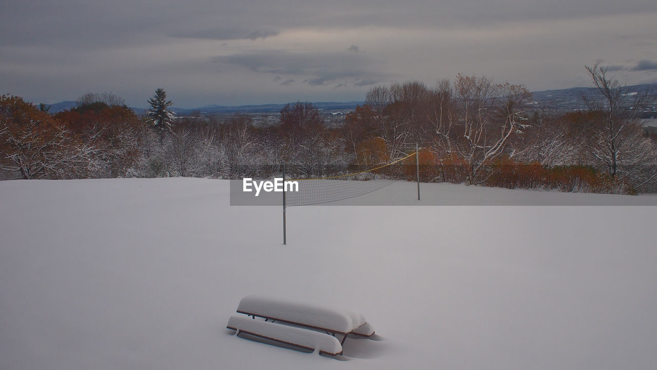 Bench covered with snow in snowy field against sky