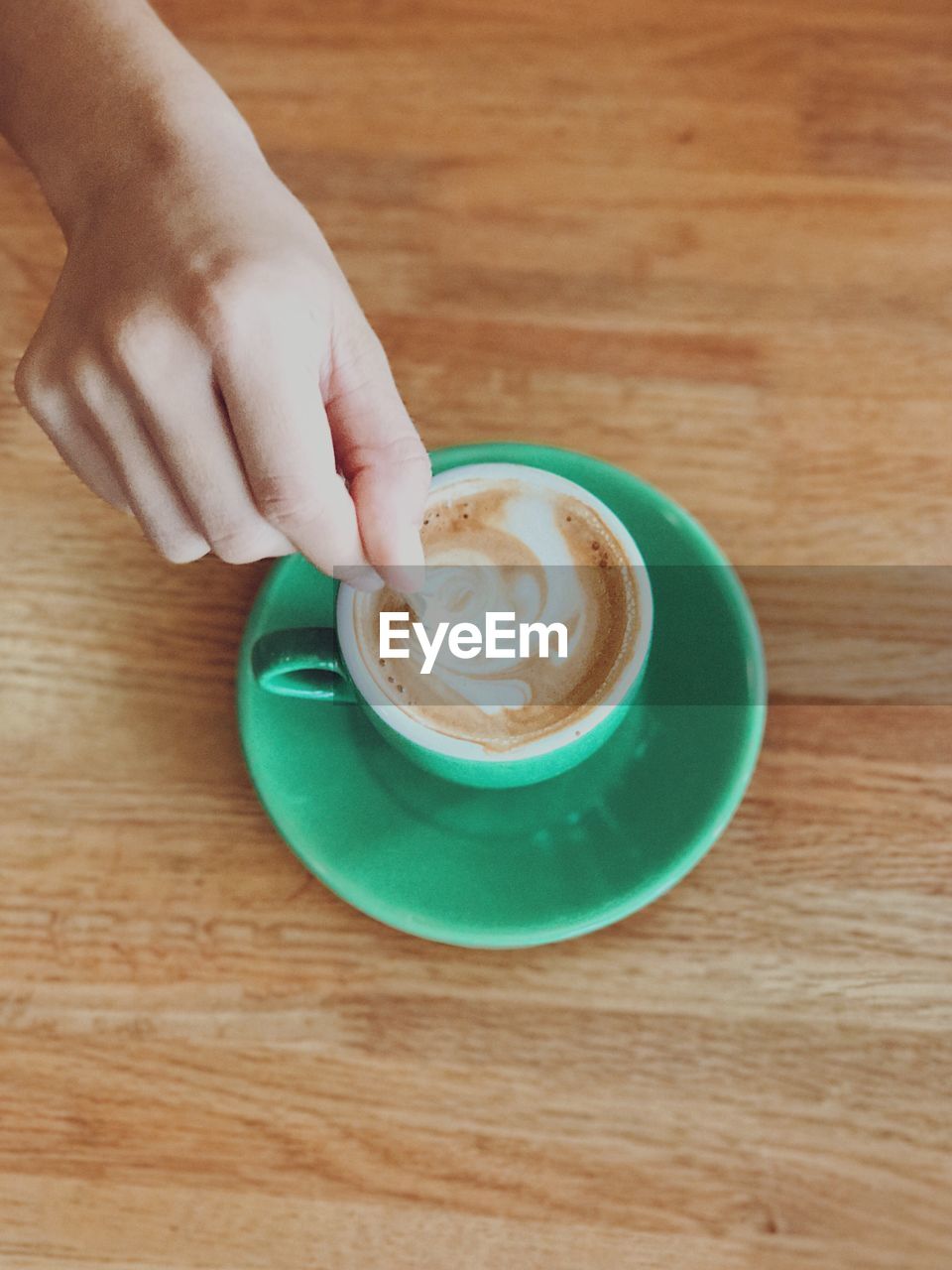 Directly above view of hand holding coffee cup on table