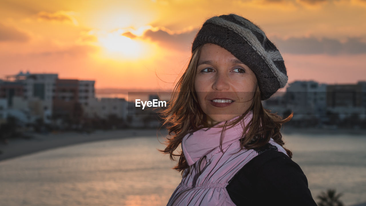 Angry woman by sea in city against sky during sunset