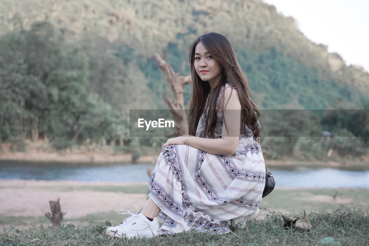 Woman in dress sitting by river against mountain