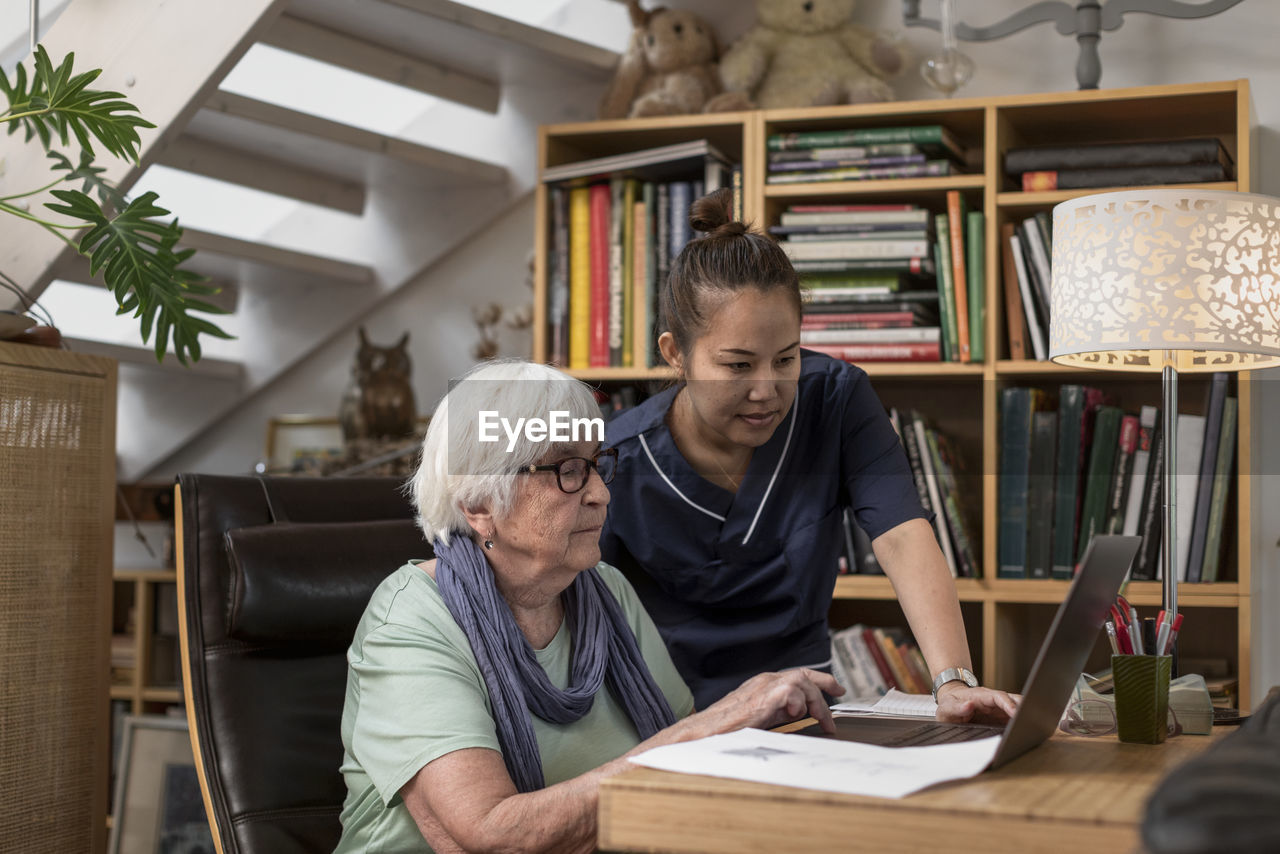 Home carer helping senior woman to use laptop