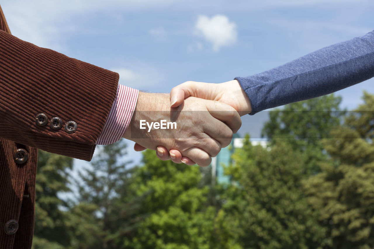 Cropped image of business people shaking hands against sky