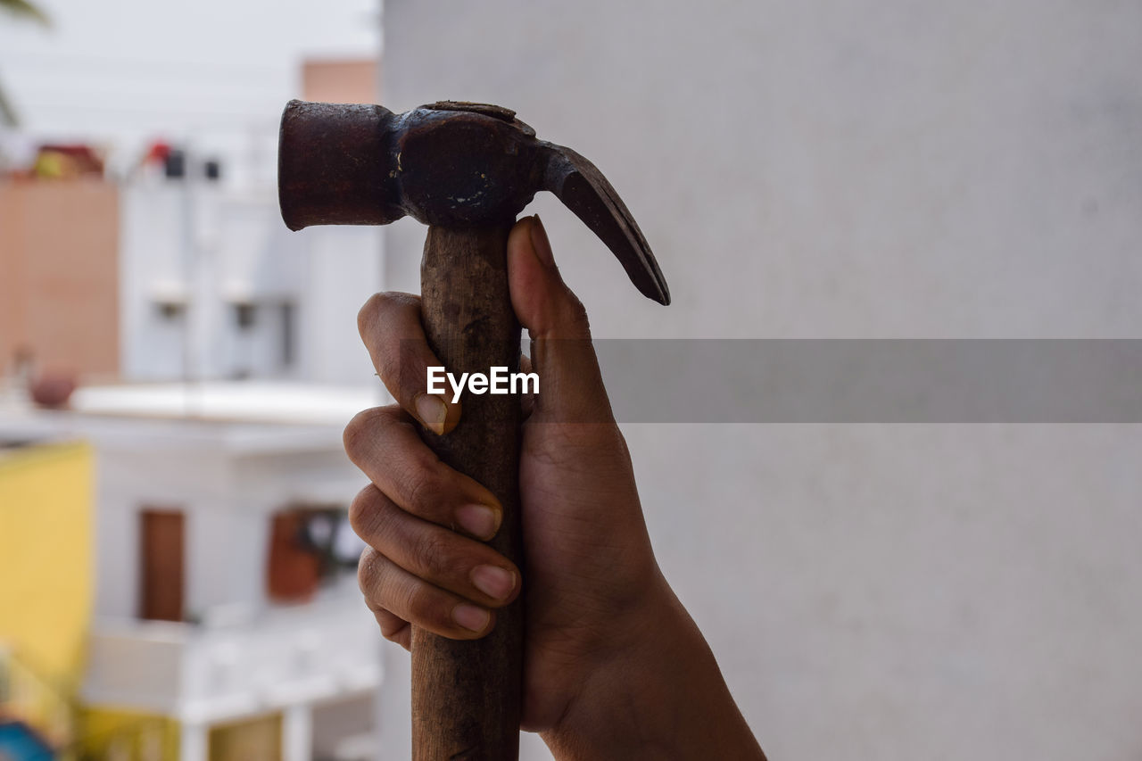 CLOSE-UP OF MAN HOLDING STICK AGAINST WALL