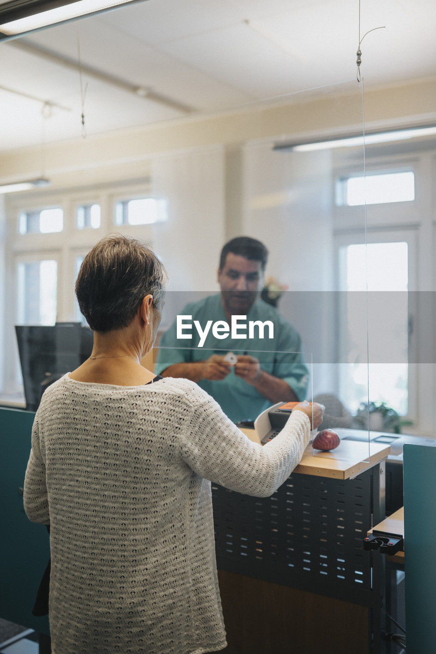 Senior female patient signing in at reception desk in hospital