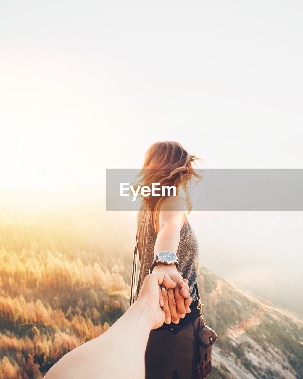 Woman holding hand on mountain against sky during sunset