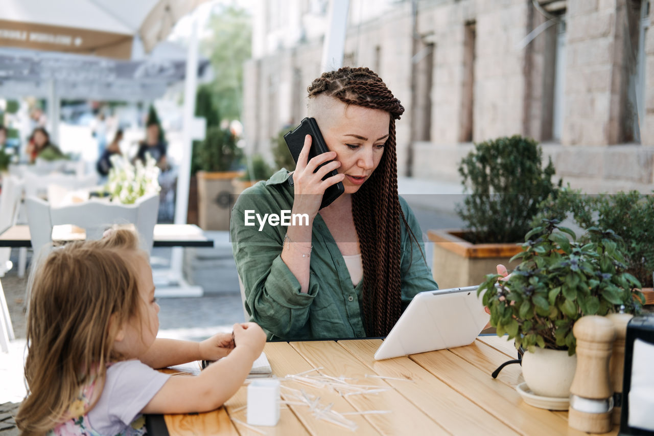 Busy successful mother and business owner with cell phone and tablet having breakfast with her