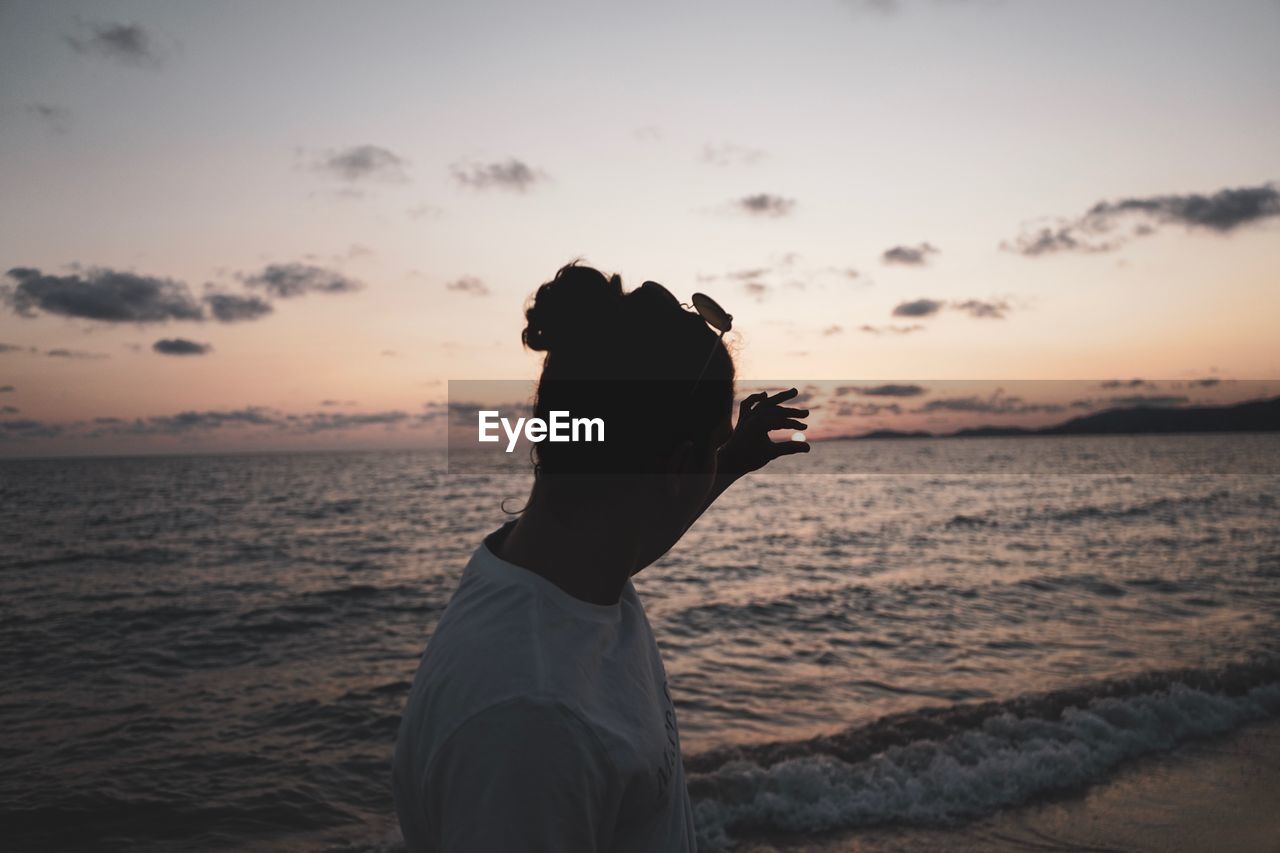 Optical illusion on young woman holding sun at beach against sky during sunset