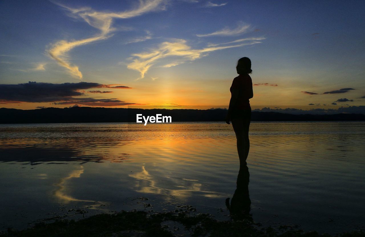 Silhouette woman standing against sea during sunset