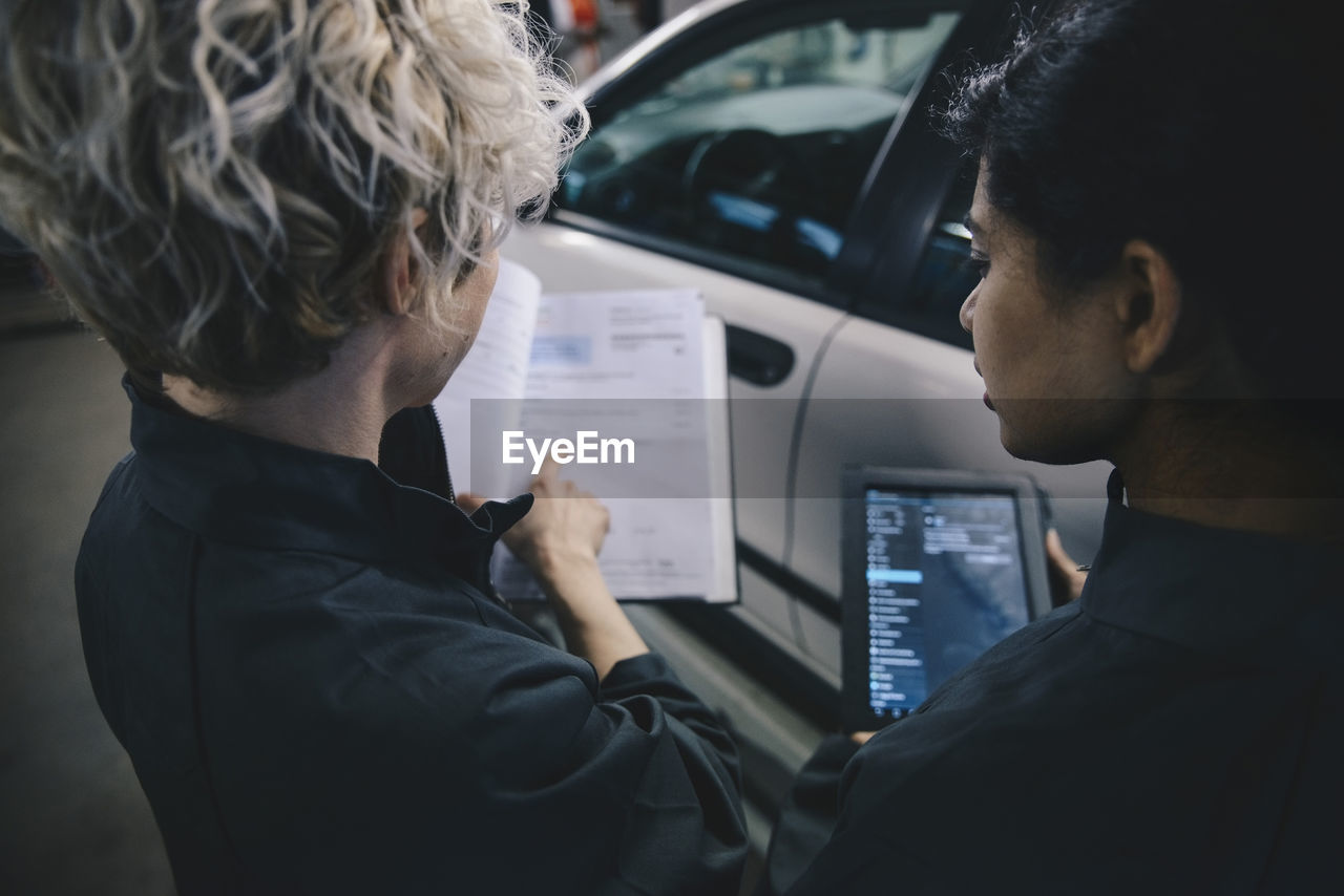 High angle view of female explaining coworker over diary in auto repair shop