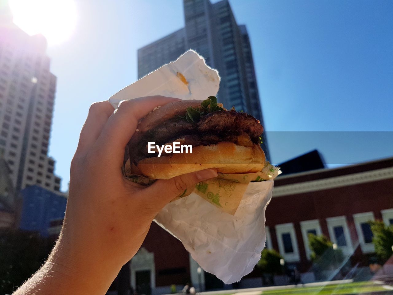 Person holding hamburger against skyscrapers 