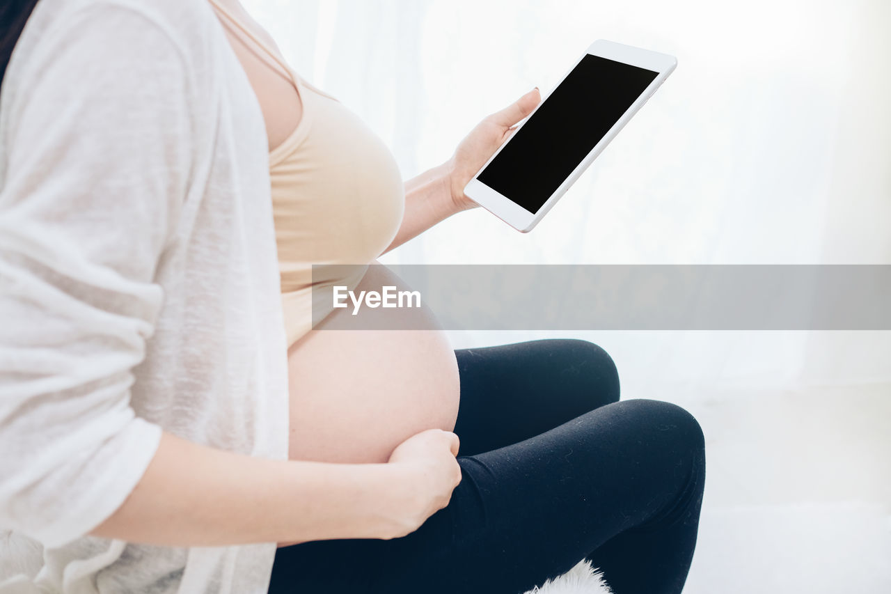 Midsection of pregnant woman holding digital tablet at home