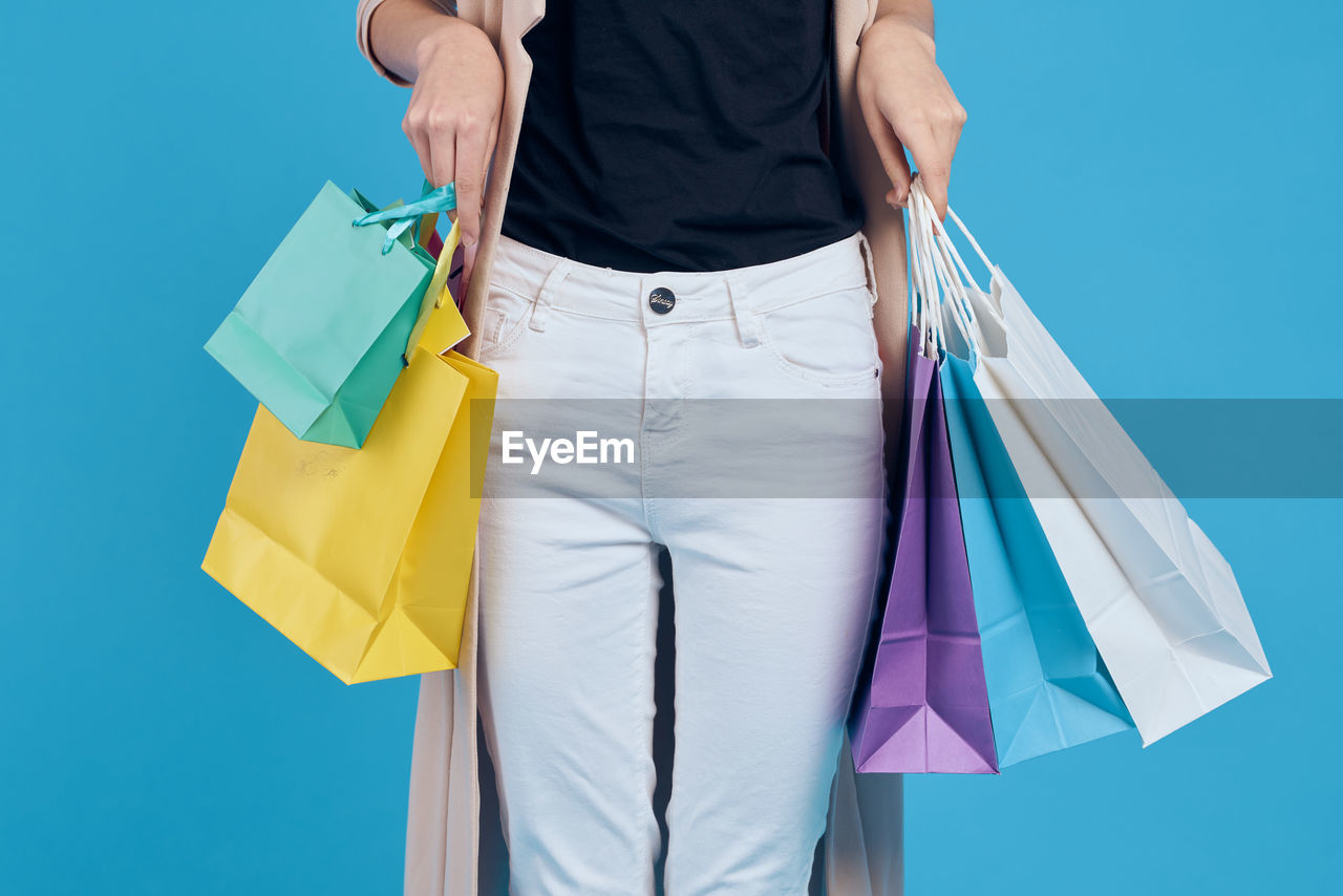 Midsection of woman holding umbrella against blue background