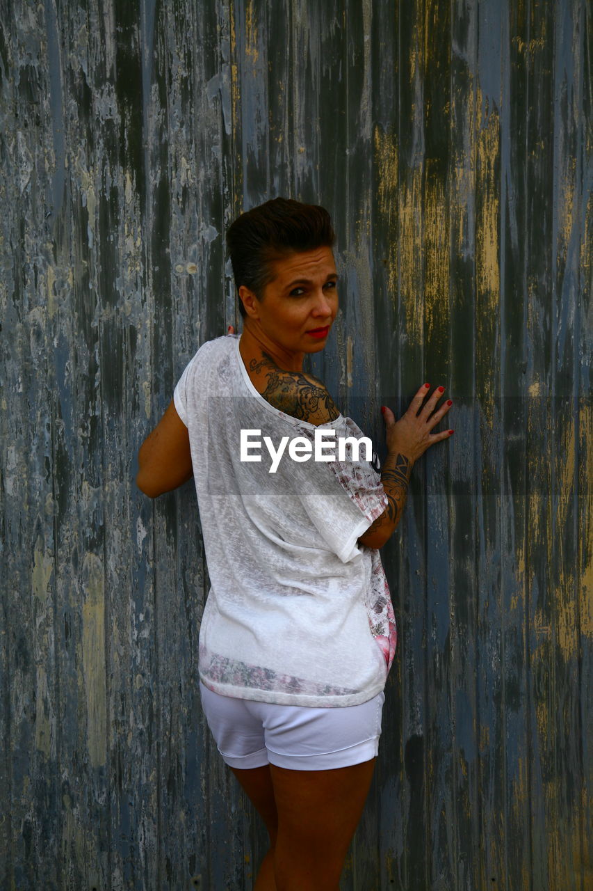 Portrait of confident mature woman standing against wooden wall