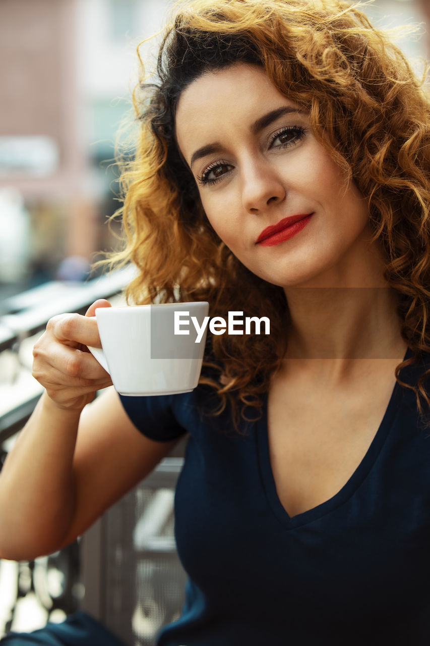 Young moroccan woman, with curly brown hair, sitting in an outdoor café in mainz, drinking coffee