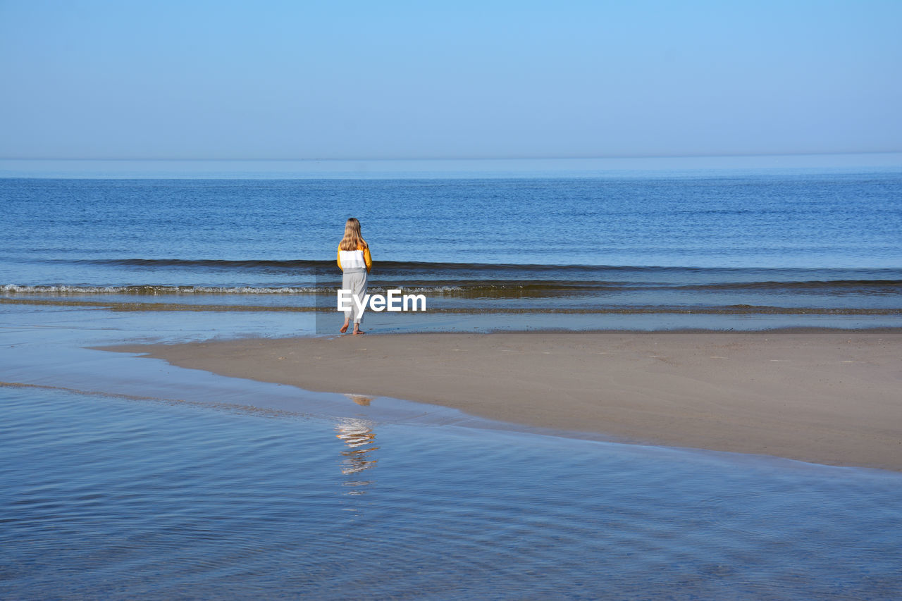 Rear view of girl walking on shore at beach against sky during sunny day