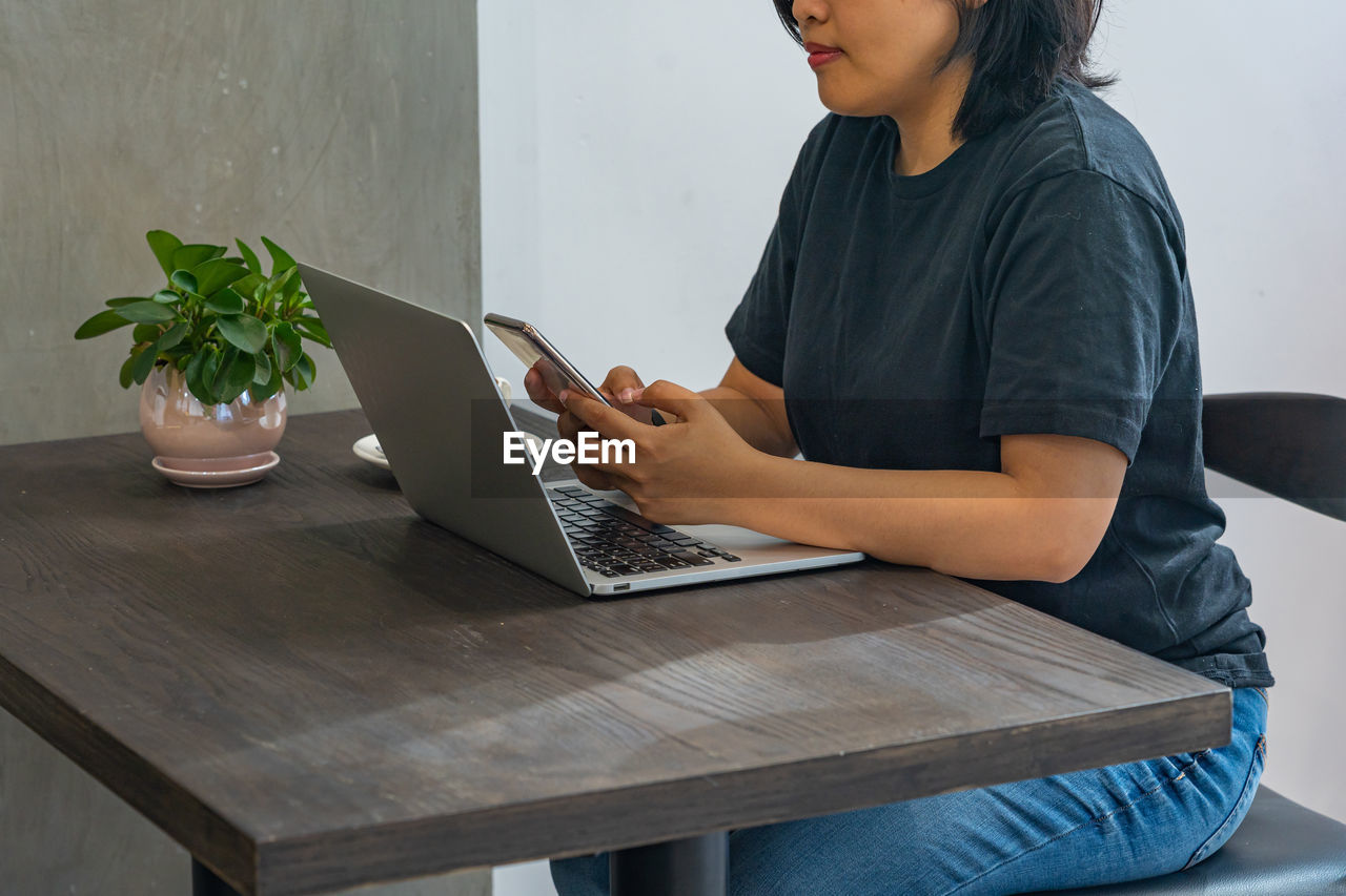 Asian woman using smartphone and working on laptop on table