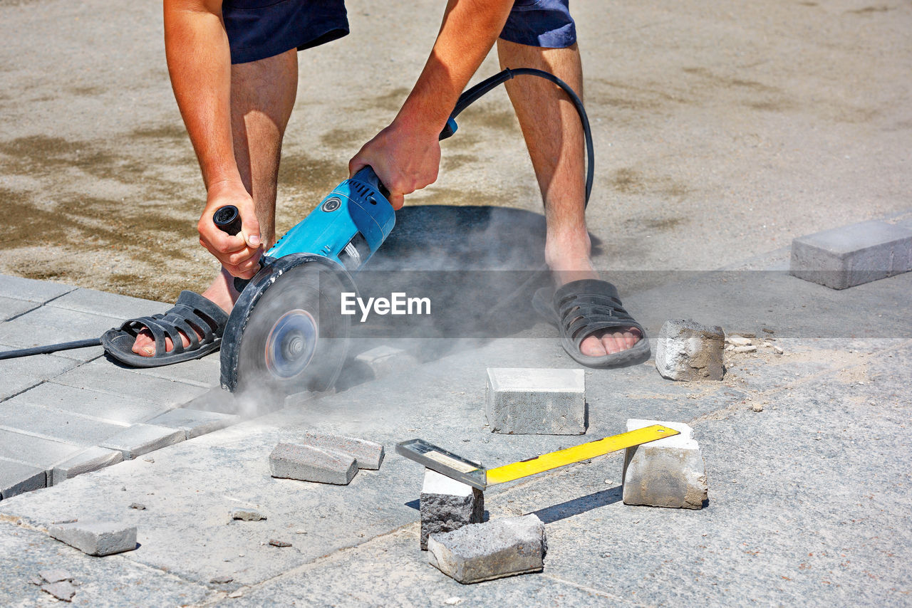 A worker cuts paving slabs with a grinder with a diamond cutting disc on a summer afternoon.