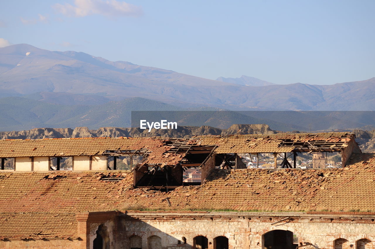 Abandoned buildings with birds on roof against mountain range