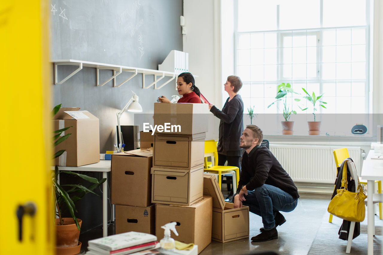 Multi-ethnic colleagues working by cardboard boxes stack at creative office