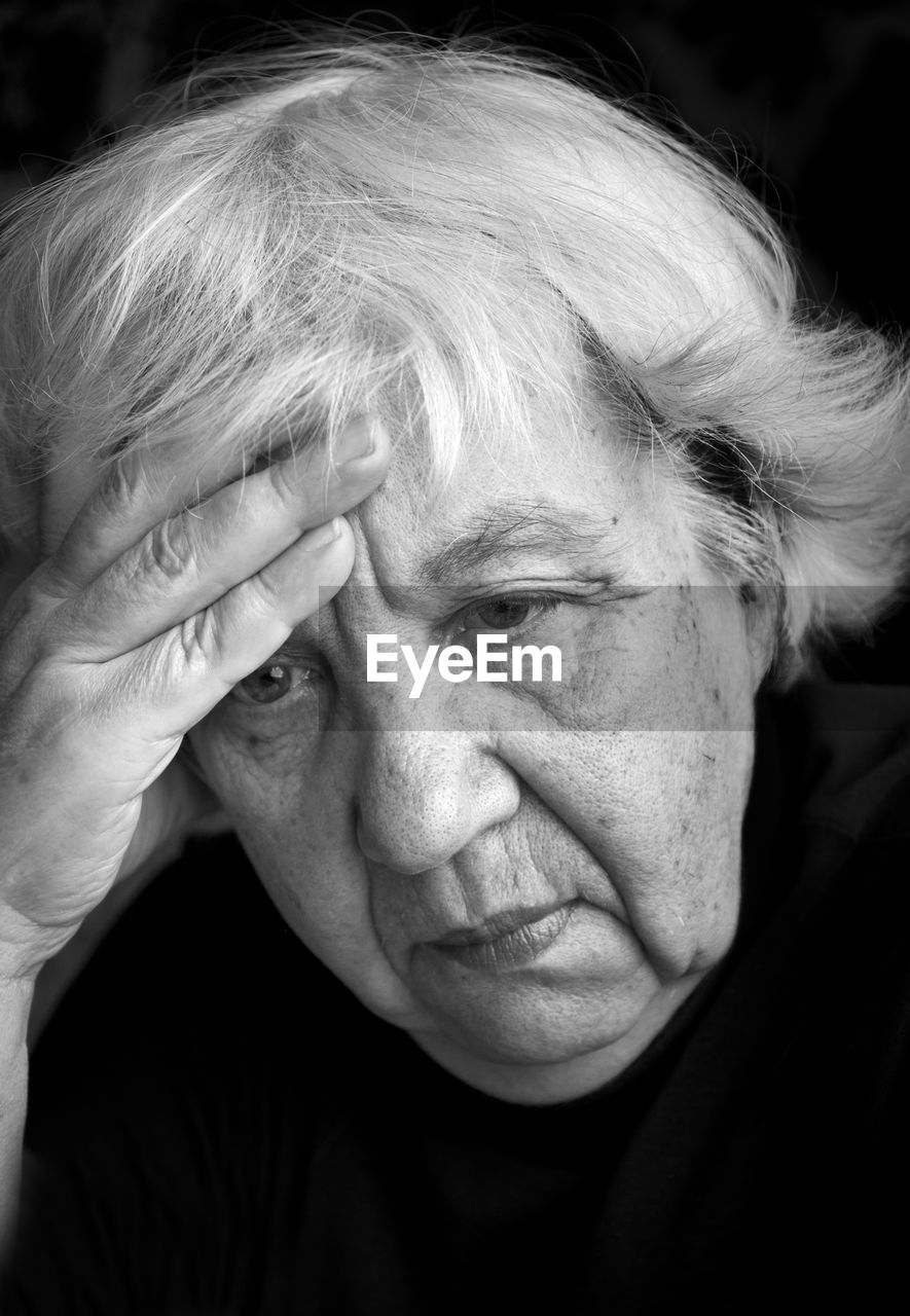 Sad senior woman against black background