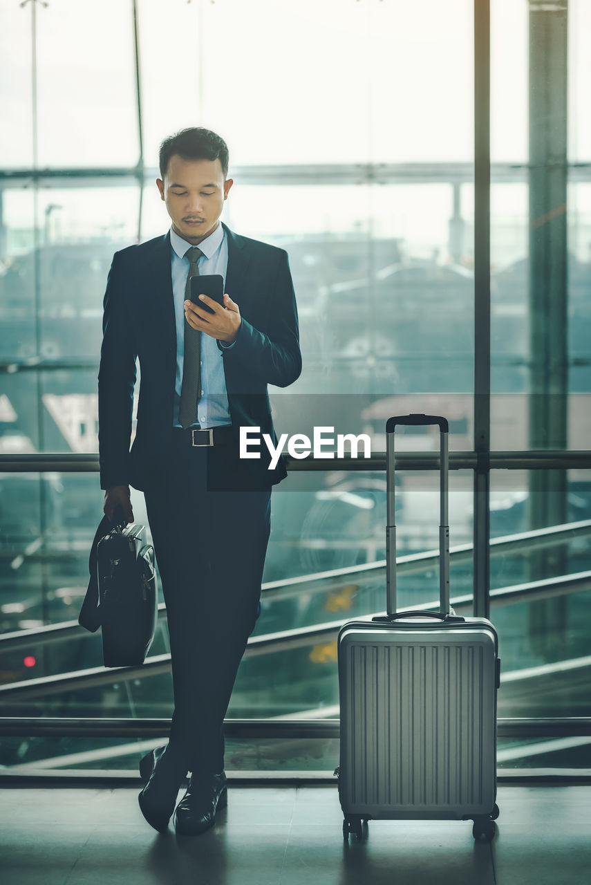 Full length of businessman using mobile phone in airport