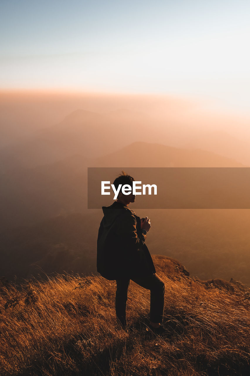 Man standing on cliff against sky during sunset