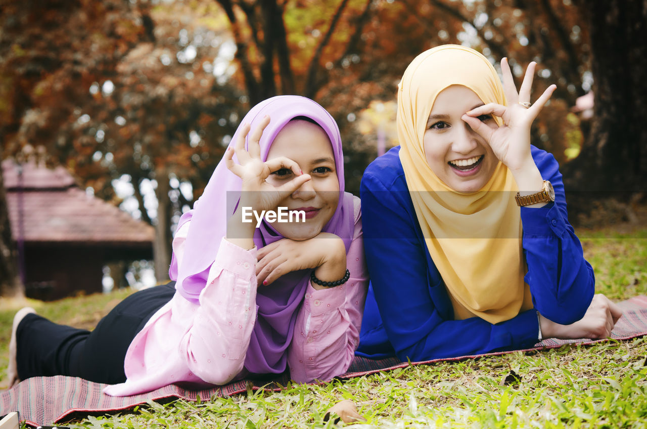  friendship and happiness concept. portrait of smile young muslimah laying on grass at city park