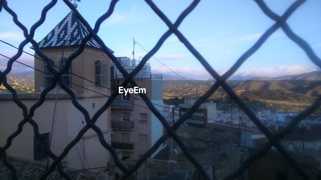 BUILDINGS AGAINST SKY SEEN THROUGH FENCE