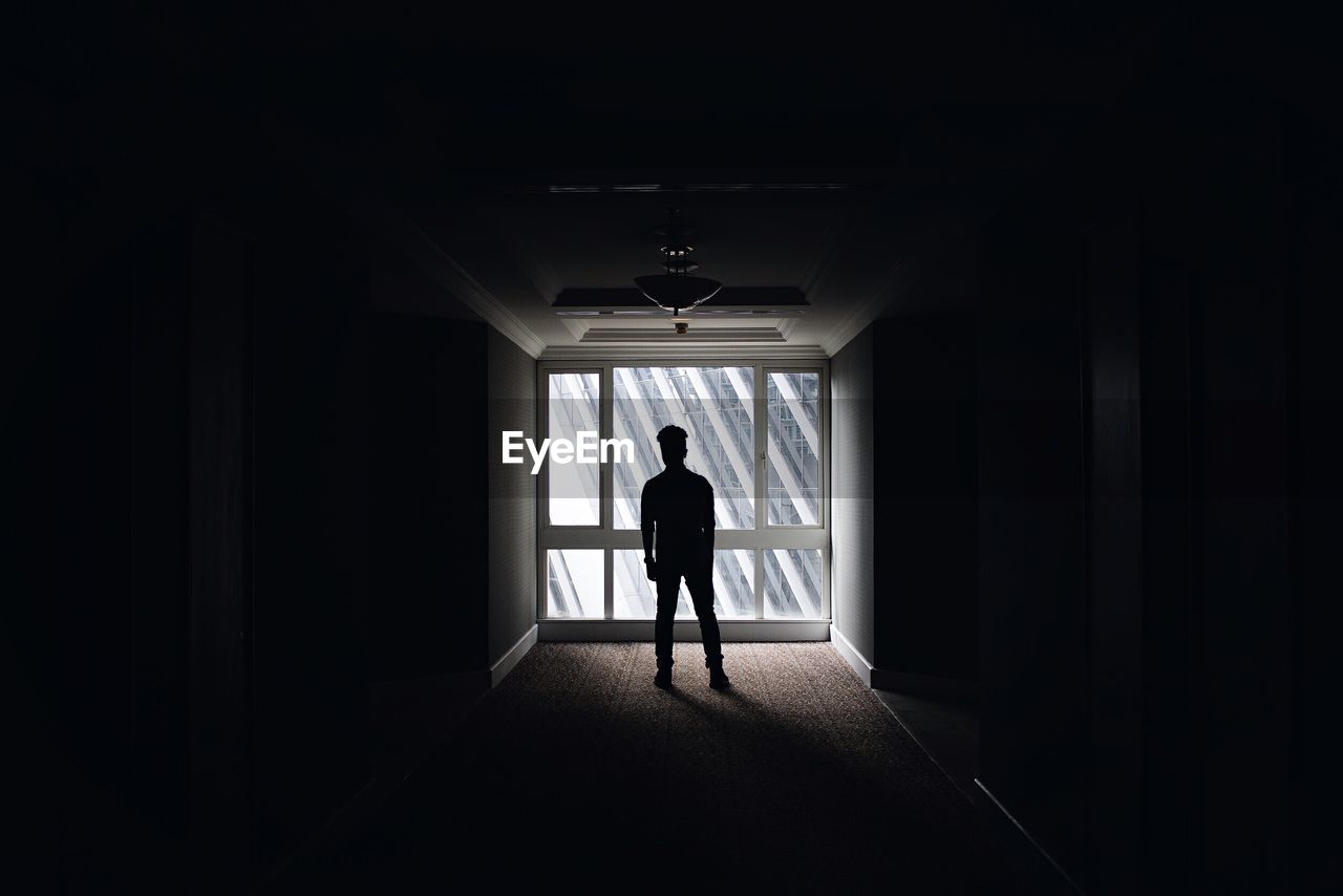 Silhouette man standing in dark corridor against window