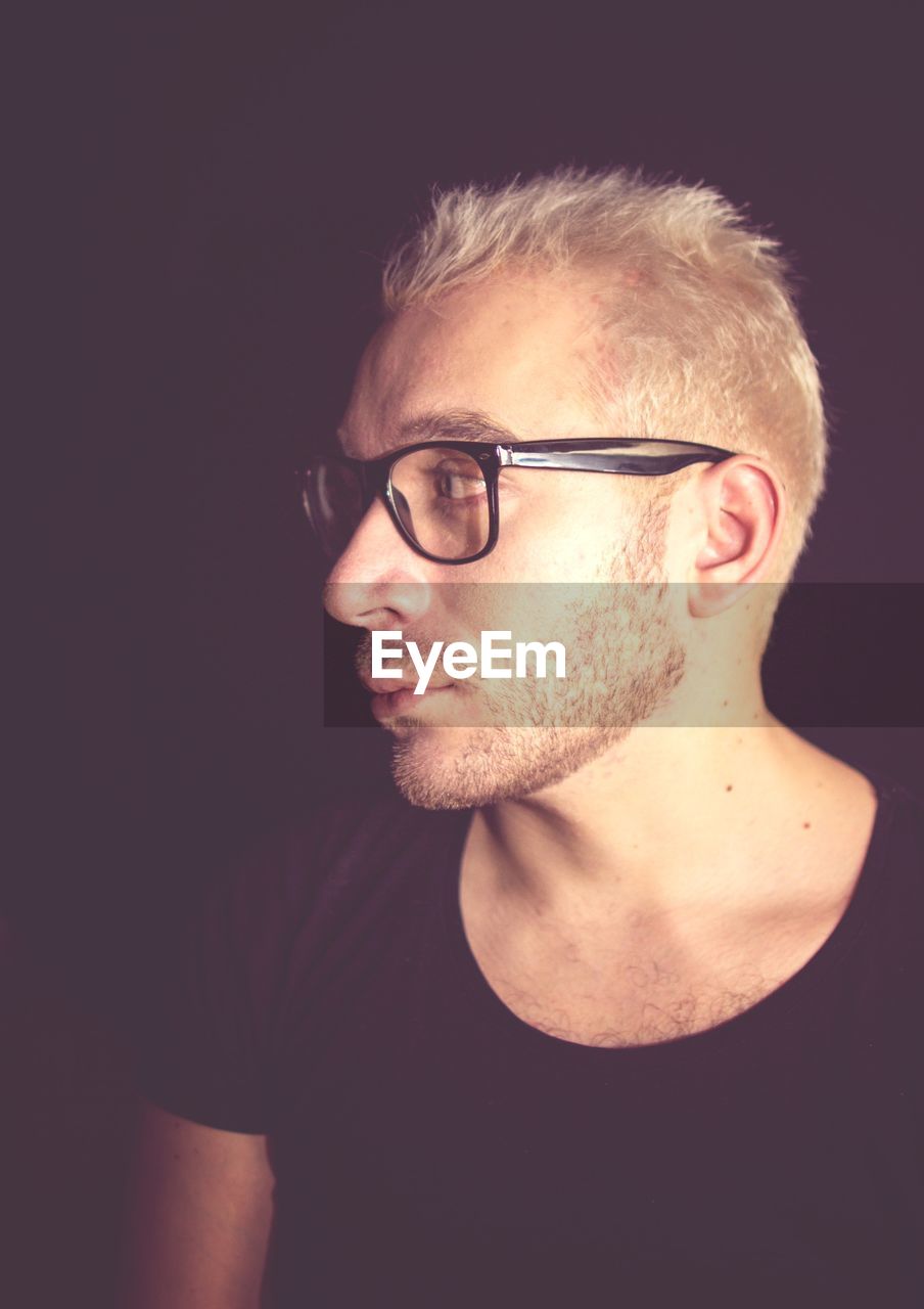 CLOSE-UP PORTRAIT OF YOUNG MAN WITH EYEGLASSES AGAINST BLACK BACKGROUND