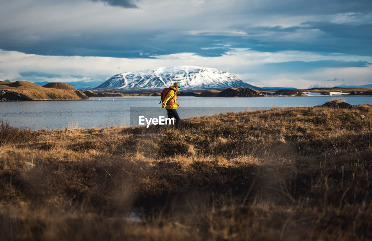 Woman walking through field next to lake with mountains in distance