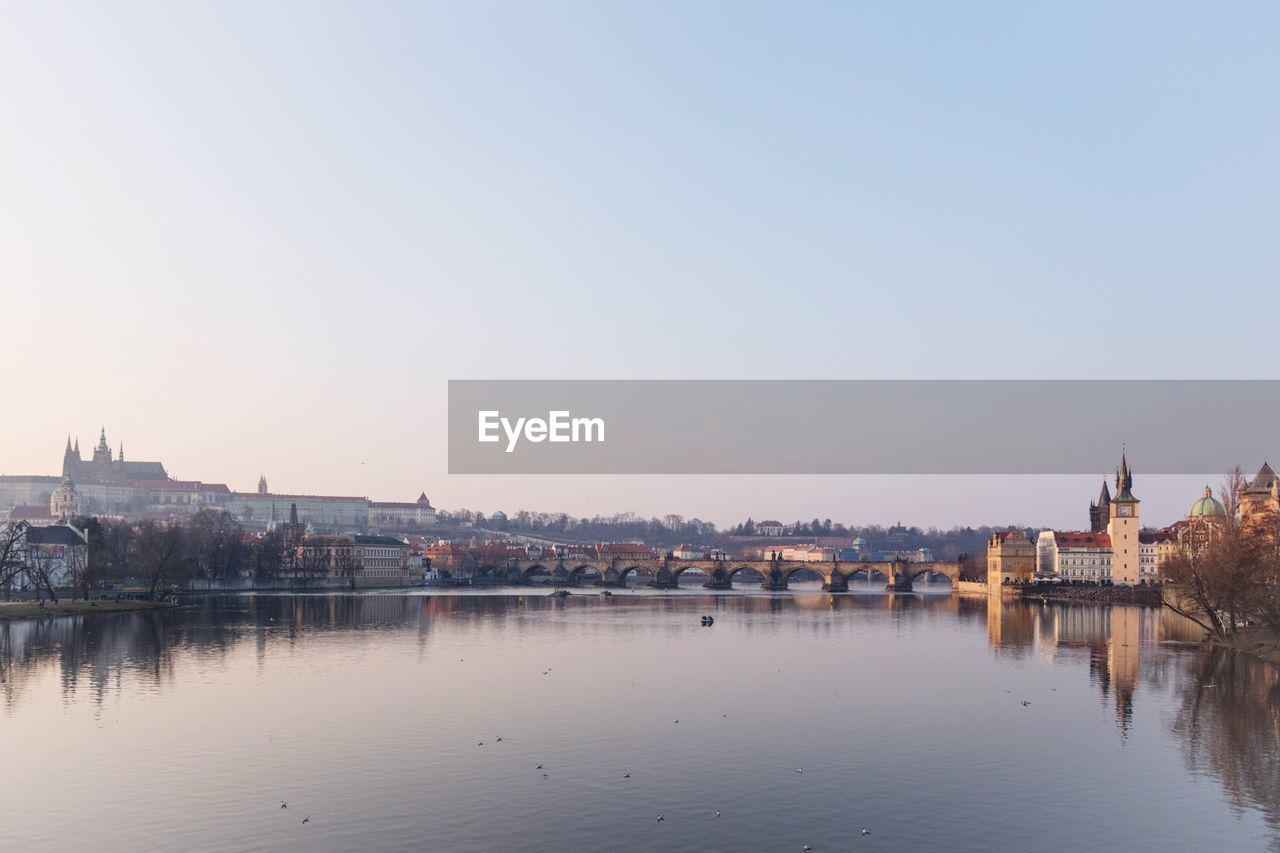 Buildings by river against clear sky