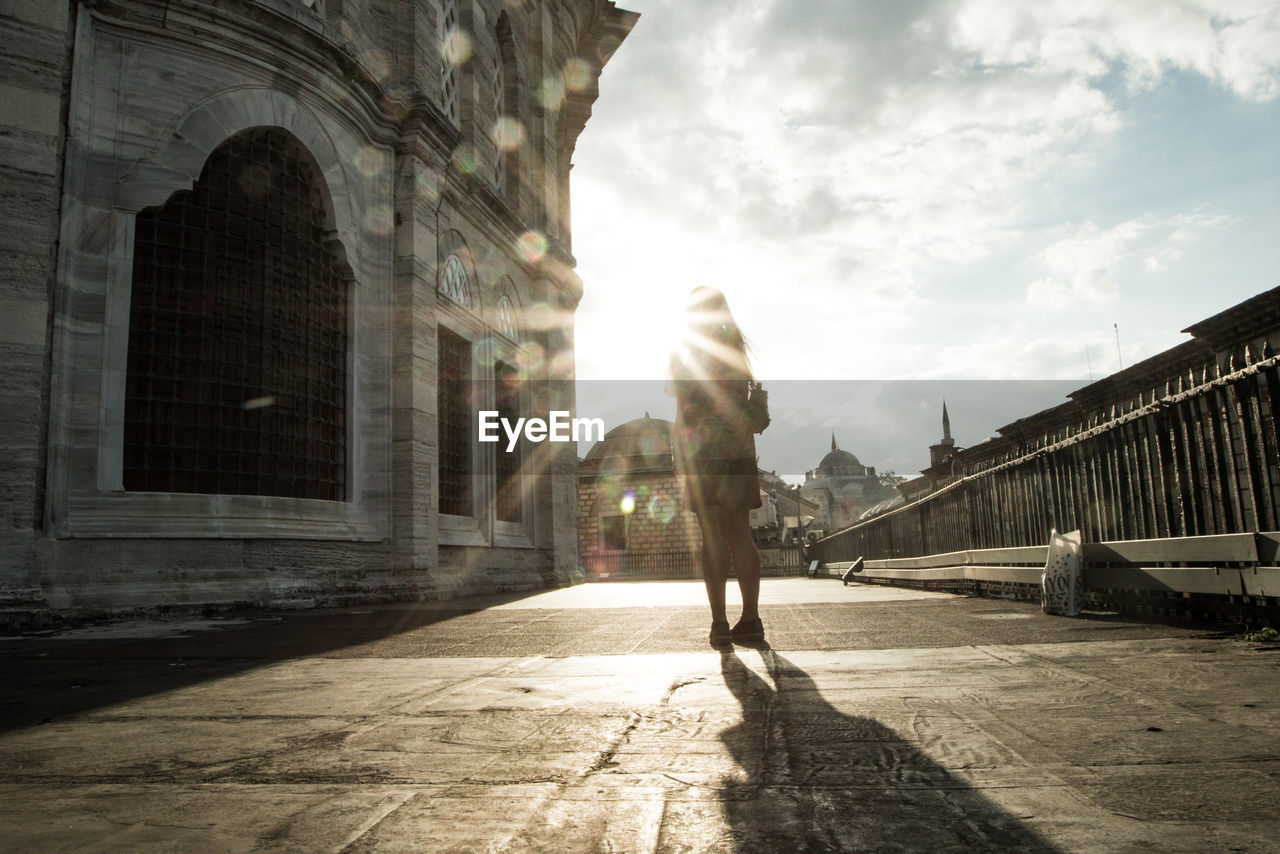 Woman walking by buildings in city against sky 