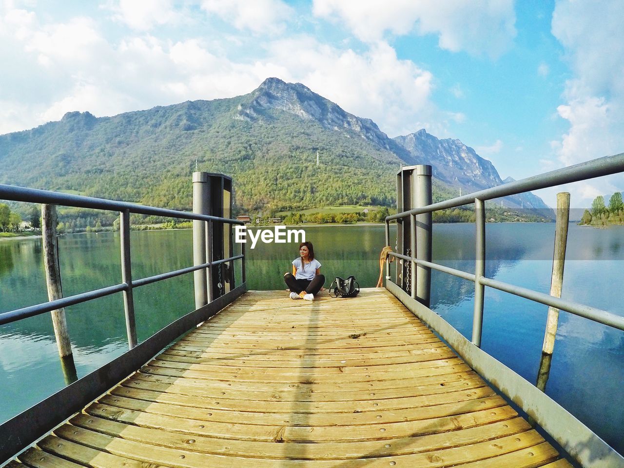 Smiling woman sitting on pier over lake against mountains