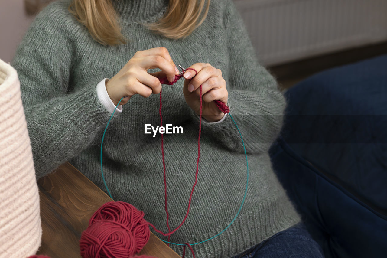 Caucasian pregnant female knits sitting in chair,woman wears warm woolen clothes