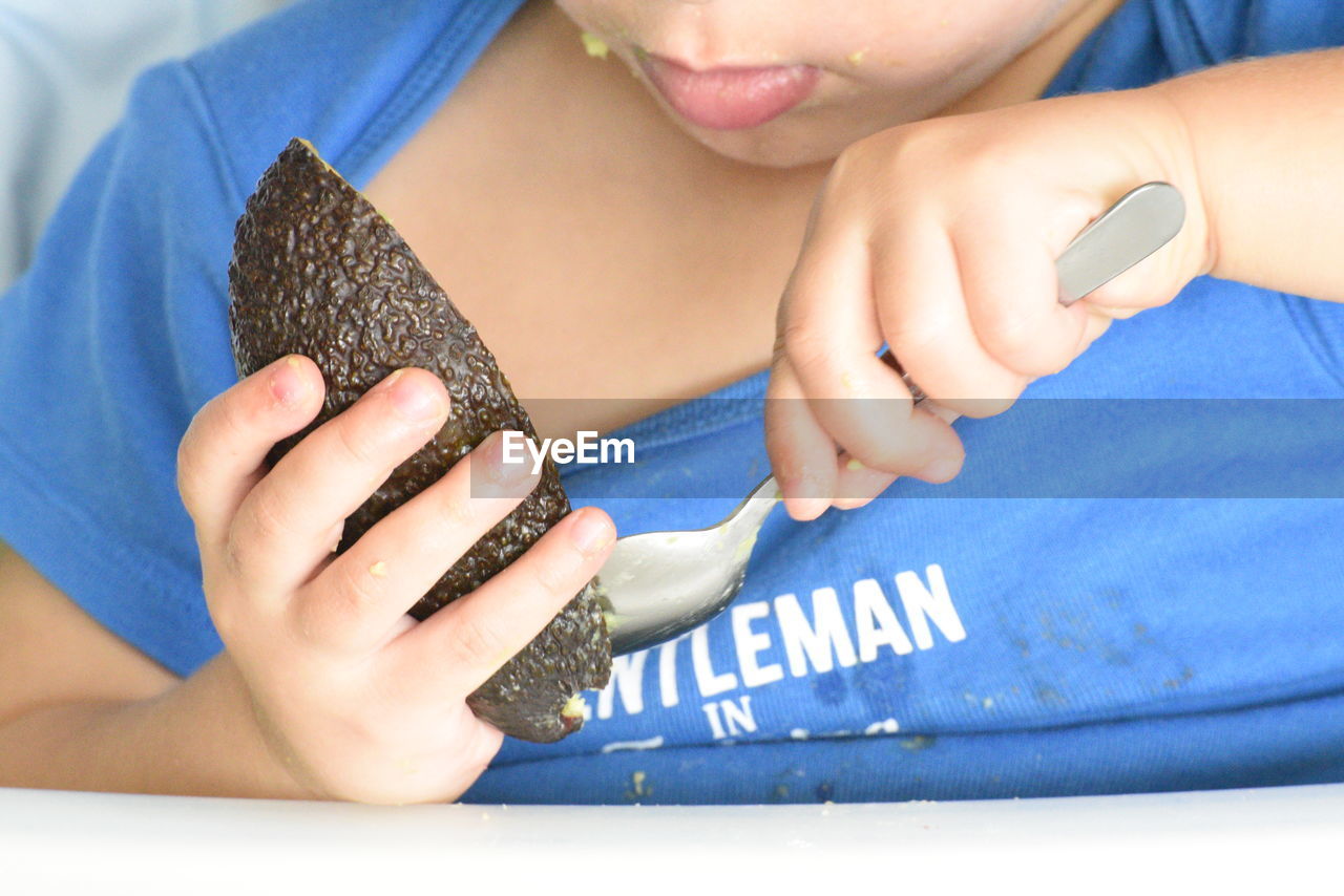 Midsection of girl eating avocado at table