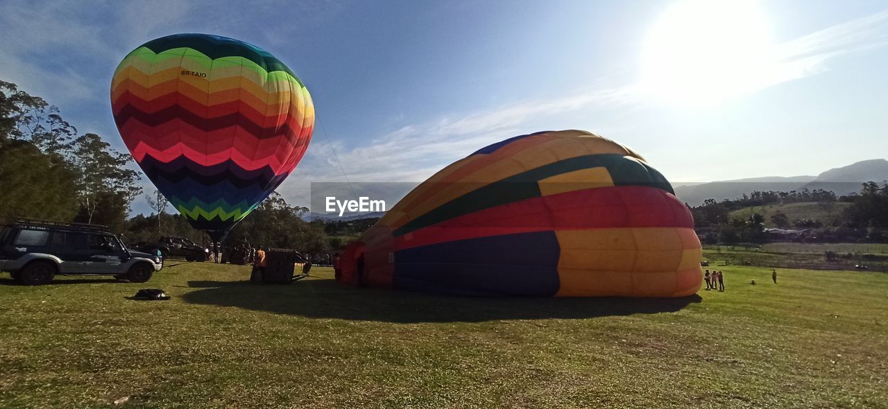 hot air balloon, vehicle, hot air ballooning, balloon, aircraft, air vehicle, transportation, mode of transportation, adventure, multi colored, toy, ballooning festival, sky, nature, flying, travel, mid-air, cloud, recreation, taking off, environment, leisure activity, burning, sports, morning, heat, flame, sun, air sports, sunlight, fire, dawn, journey, executive car, inflating, vacation, trip, twilight, landscape, tourism, grass, basket, travel destinations, car, plant, outdoors, holiday, celebration, outdoor pursuit, day, tradition, blue, land, traditional festival, extreme sports