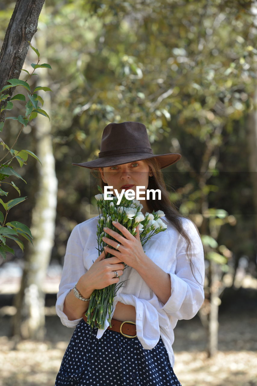 Portrait of beautiful woman holding flowers standing by trees