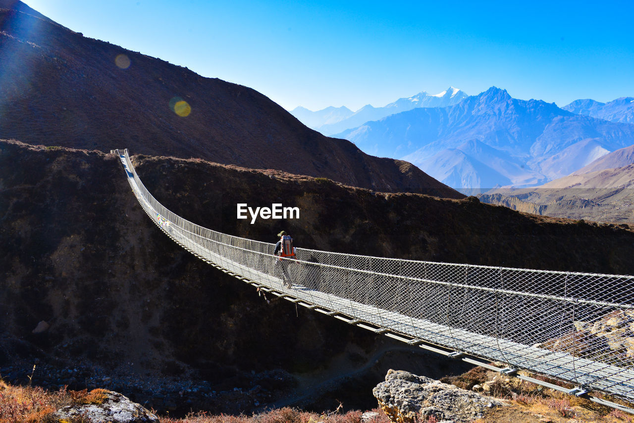 Person walking on bridge against mountains