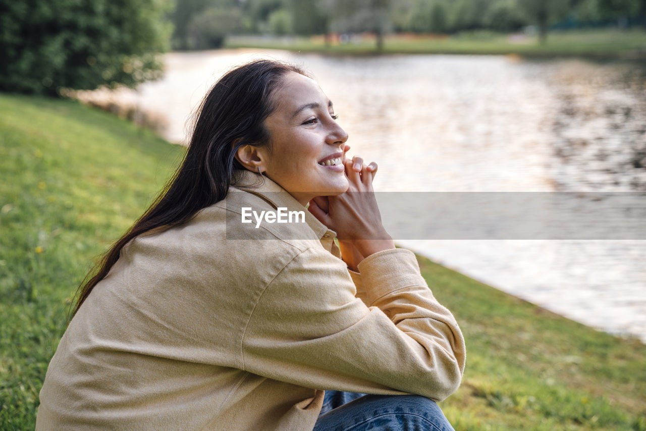 Smiling woman sitting by lake at park