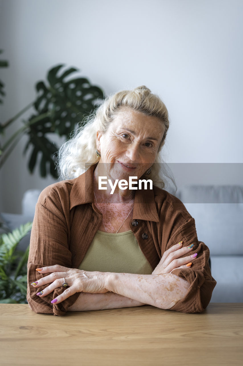 Smiling senior woman with arms crossed at home