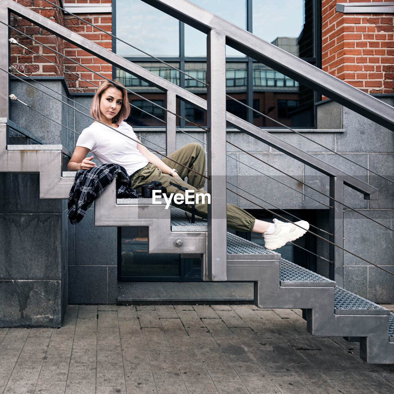 Hip hop style girl with a dslr camera  laying on metal stairs in an urban environment