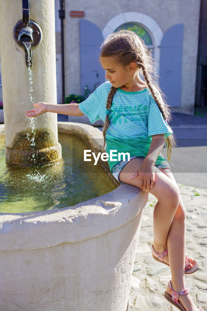 Girl puts hand in water of old fountain on the typical square of small european villages, travel