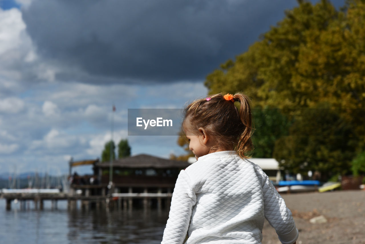 Rear view of girl standing at beach against cloudy sky