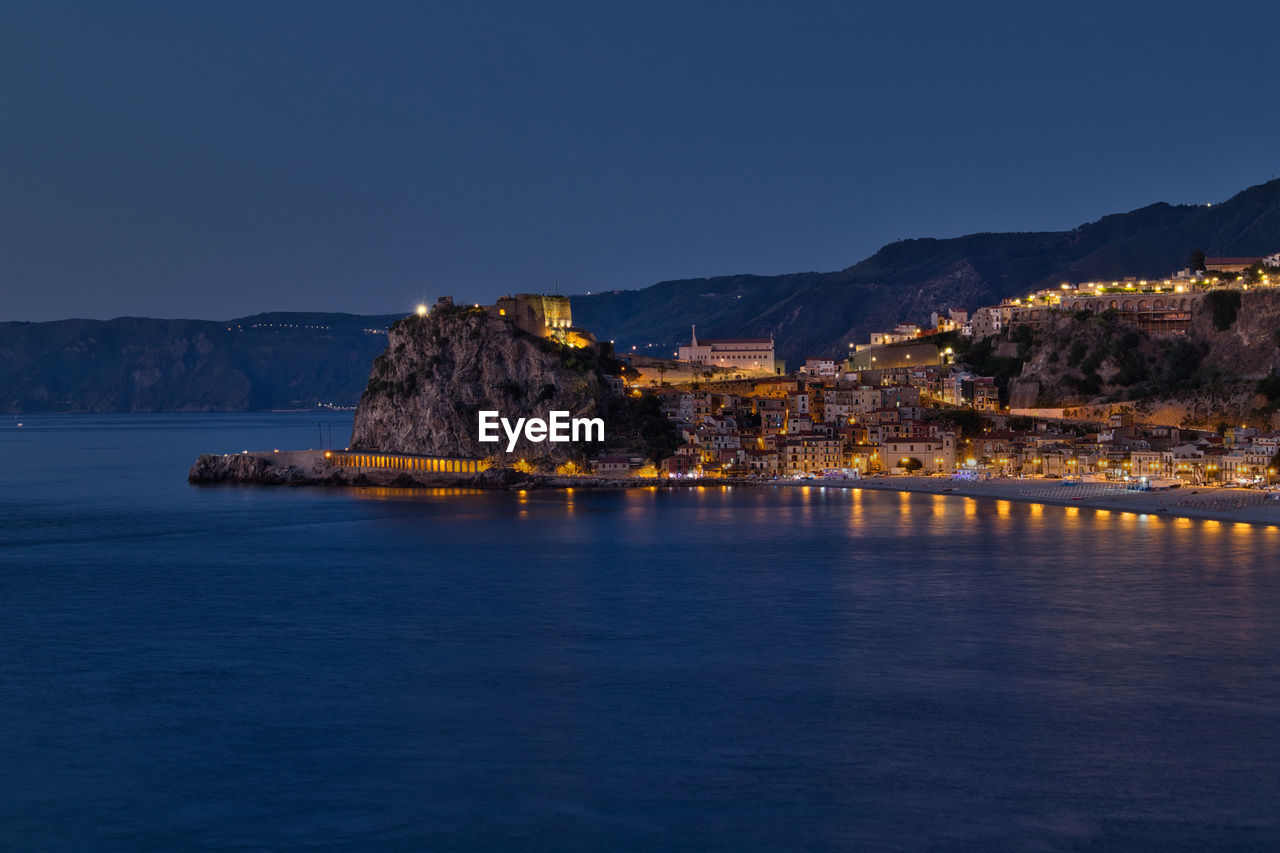 Scenic view of sea by buildings against clear blue sky