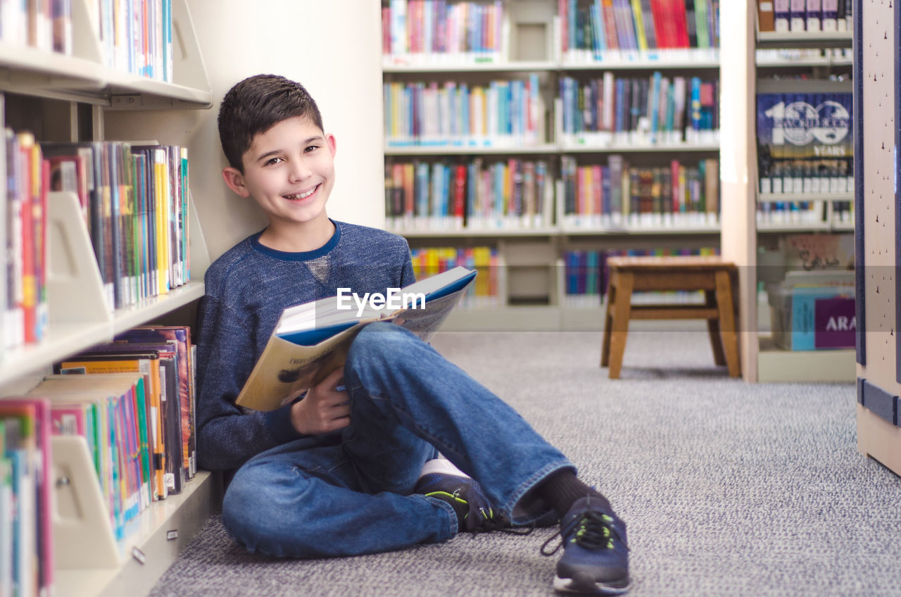 Portrait of smiling boy reading book while sitting in library